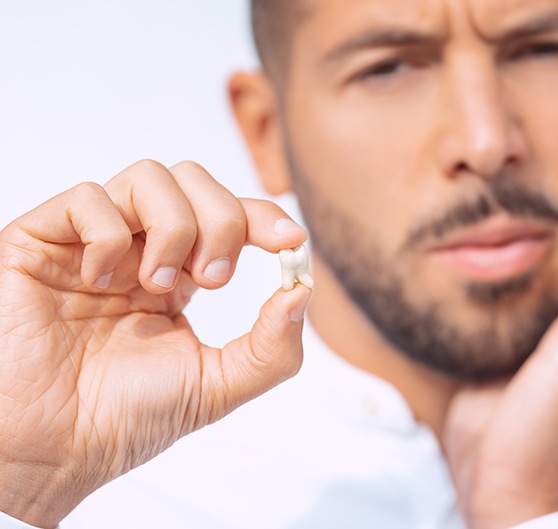 Man holding extracted tooth with one hand and his sore jaw in the other