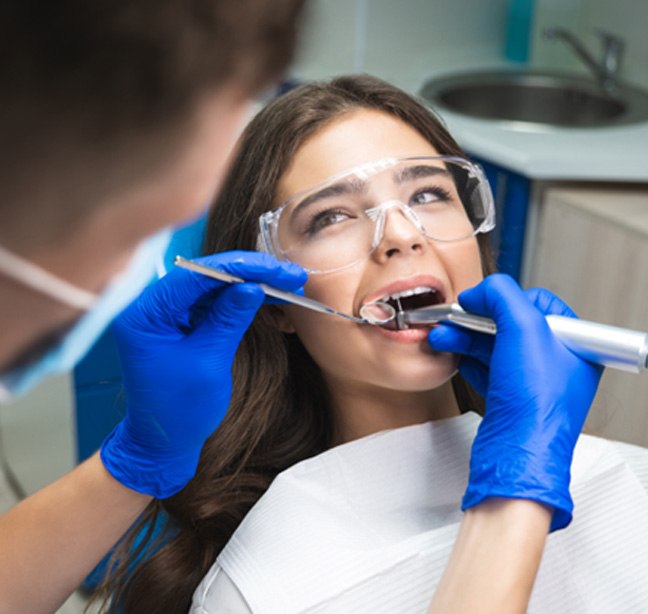 Woman in safety goggles having root canal performed by dentist in blue gloves