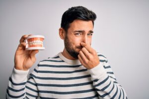 Man in striped sweater holding model teeth and plugging his nose